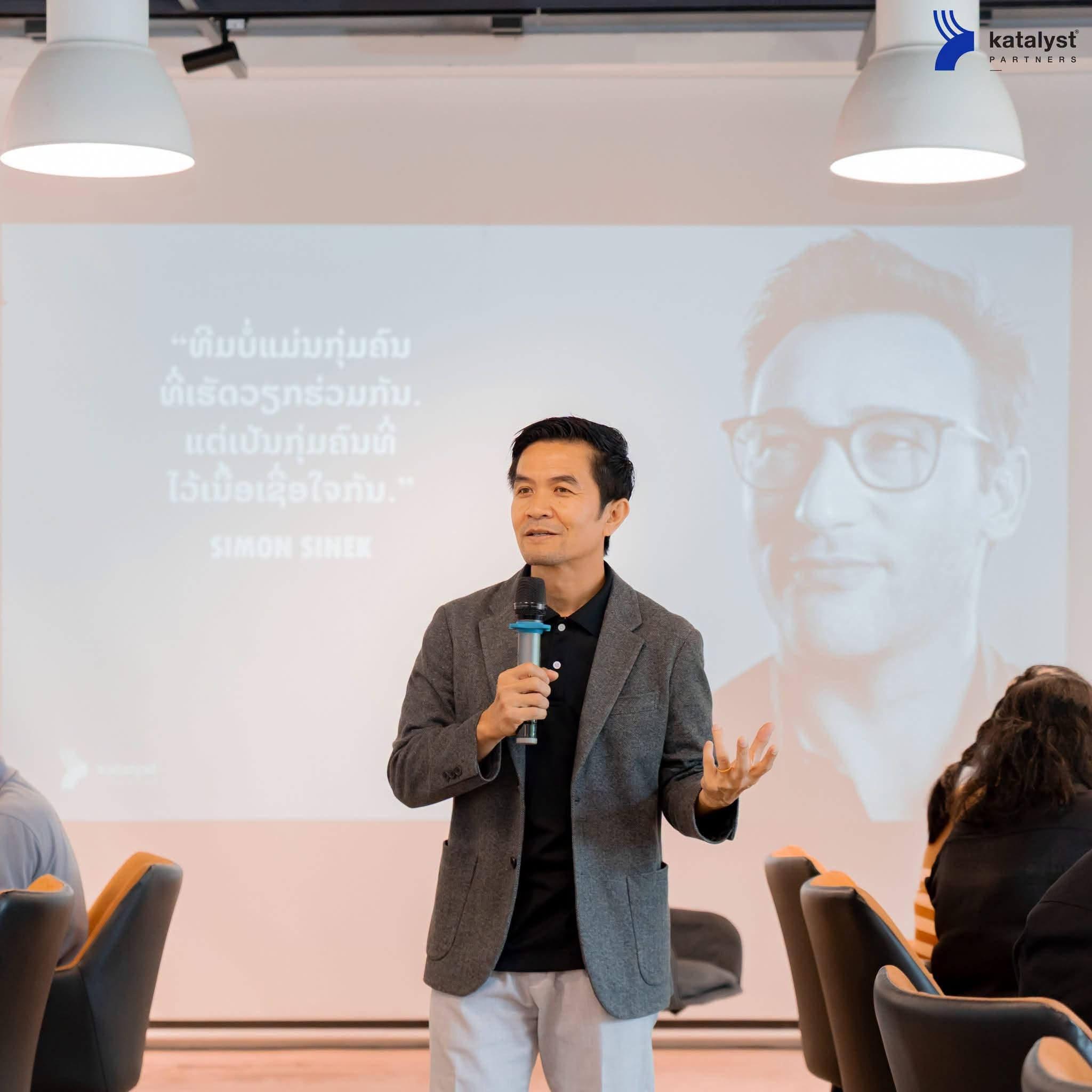 A Katalyst facilitator leading a workshop beside a Lao-language Simon Sinek quote.