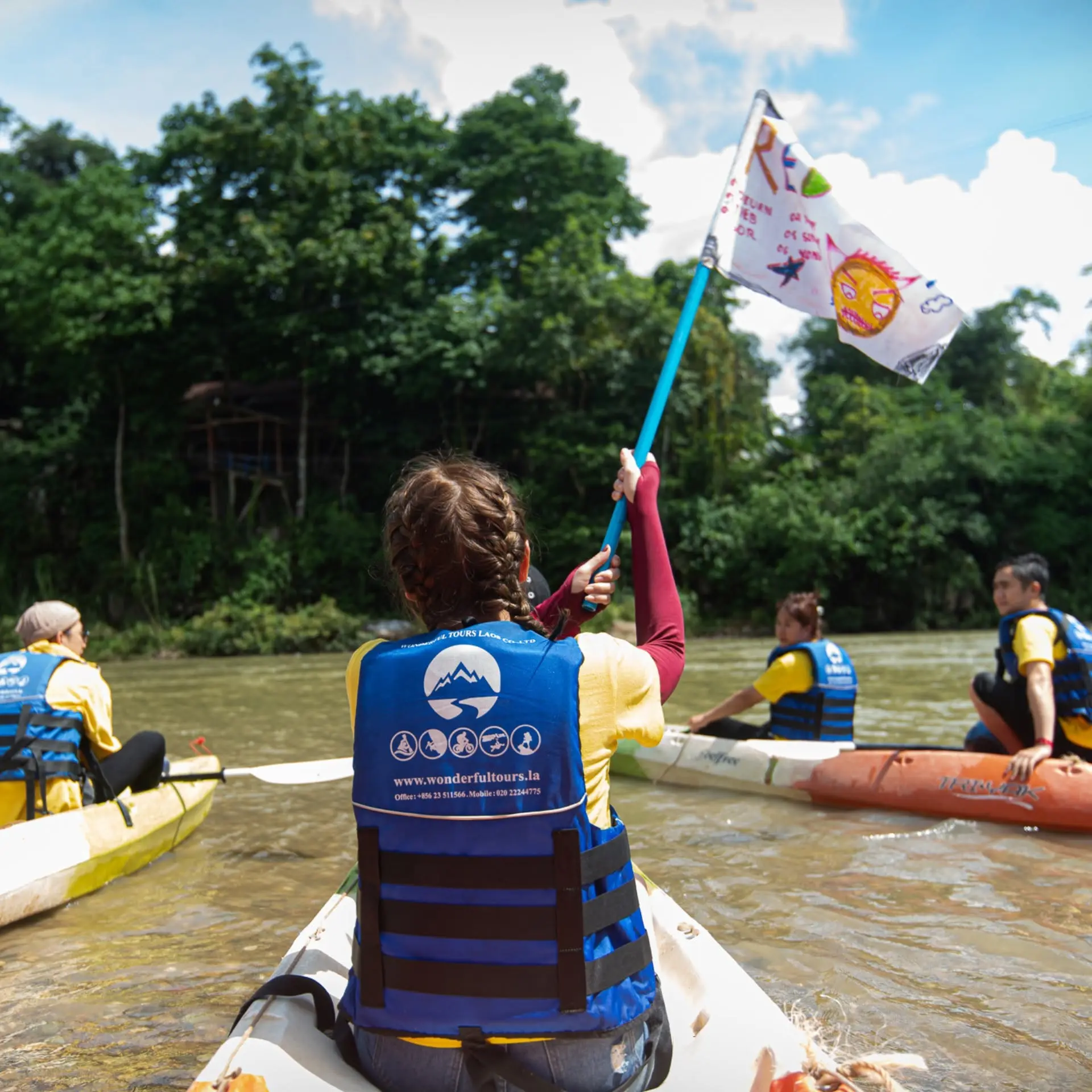 Amazing Race participants kayaking with their team flag in Vang Vieng